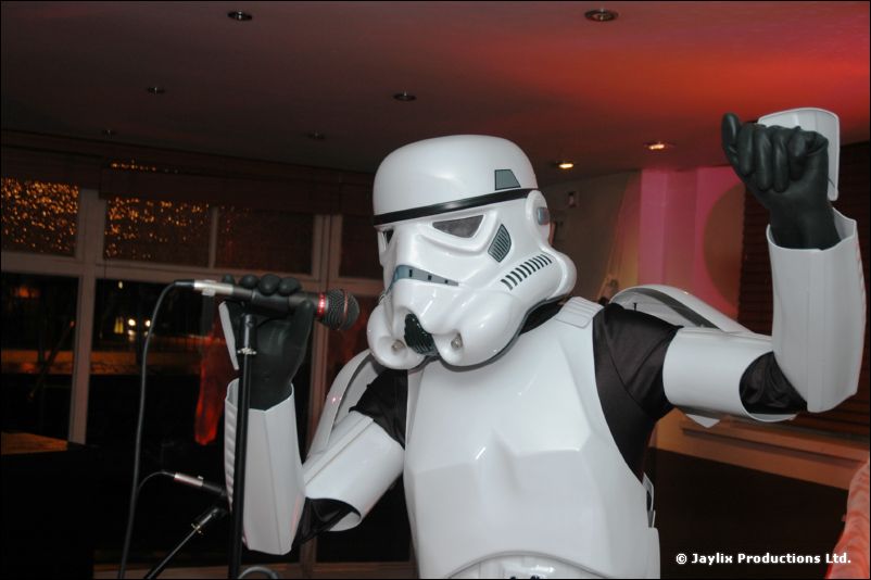 A stormtrooper costume raises a gloved fist beside a microphone stand