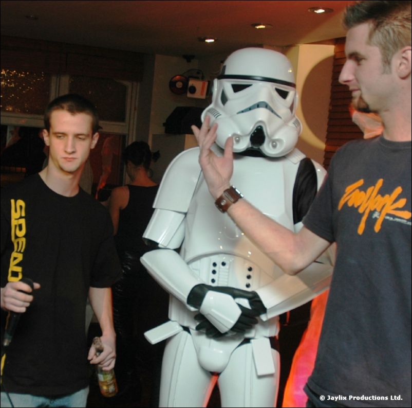 A stormtrooper costume stands between two young men in a busy bar