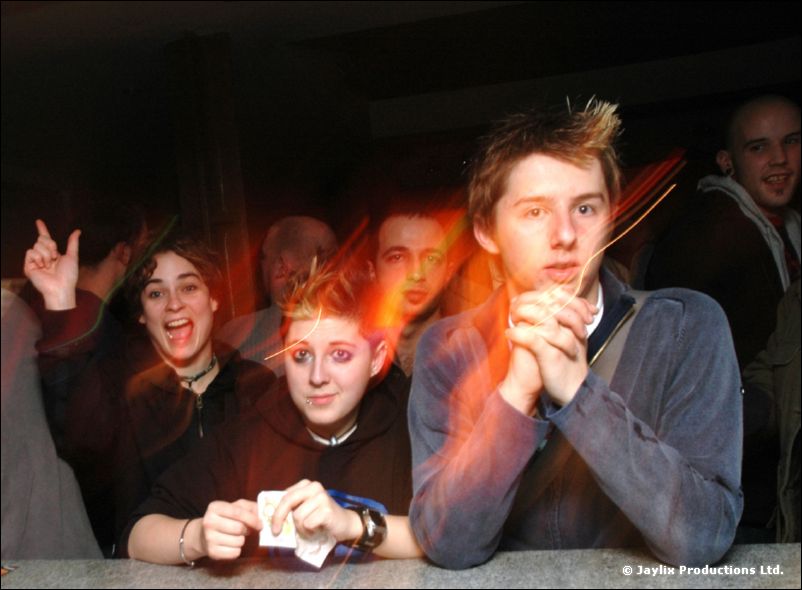 Several young people lean on a bar counter, some pulling faces, with orange light streaks