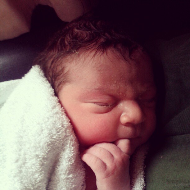 Sleeping newborn baby wrapped in a white towel with a hand near the mouth