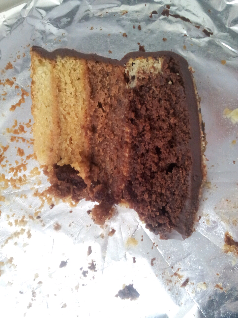 A slice of three-layer sponge cake with chocolate coating on silver foil