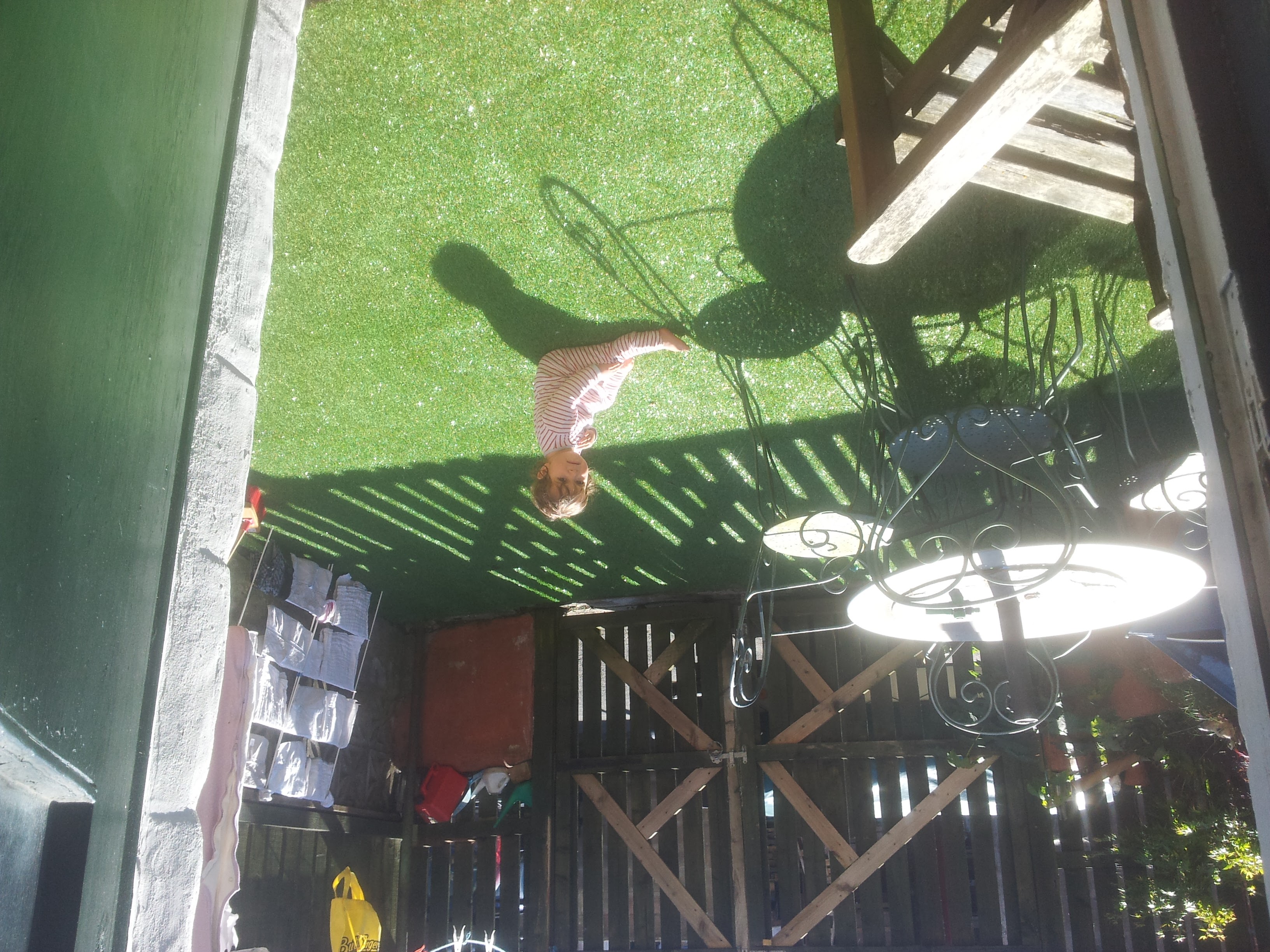A sideways view down on a garden with artificial turf, a table and chairs, and a small child in the distance