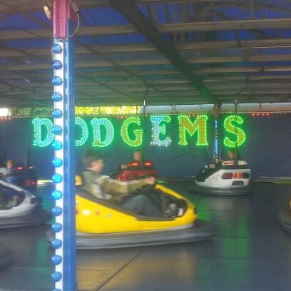 A person in a yellow dodgem car beneath a green illuminated DODGEMS sign