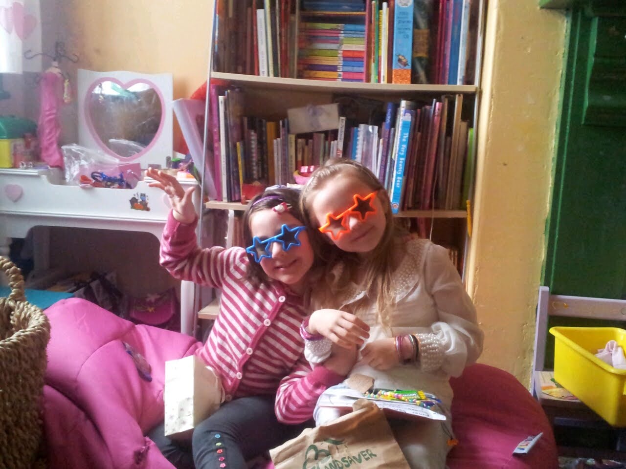 Two children in a bedroom, one wearing blue and one orange star-shaped sunglasses