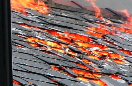 Close-up of a slate roof with flames burning through gaps