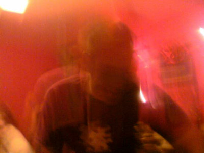 Very blurred red-lit image of a person in a dark patterned top