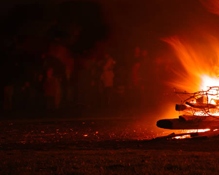Bonfire burning low at the right of a dark field