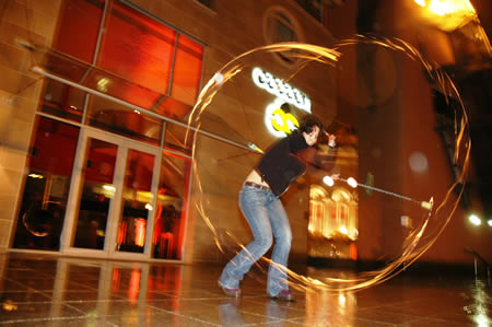 Person spins a fire staff outside a building, leaving glowing circular trails