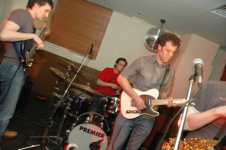 Band playing in a bar, guitarists at the front and a drummer behind with a Premier kit