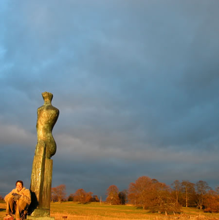 A bronze figure stands on a hill at sunset with a small seated person at its base