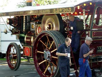 Two men in overalls drinking tea beside a red steam traction engine with Anderton and Rowlands lettering