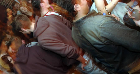 A tightly packed, blurred crowd of people in hoodies and jackets on a dance floor
