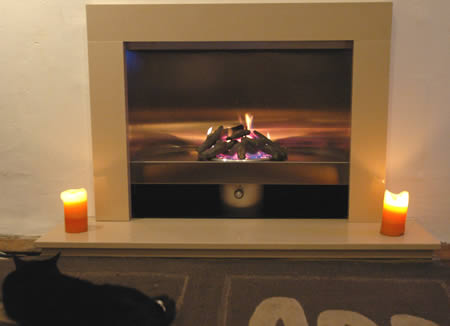 A modern gas fire in a stone surround with two candles and a black cat on the floor