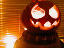 Carved pumpkin with a jagged grin glowing in front of window blinds