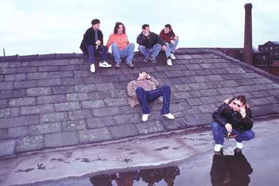 Five people sitting and crouching on a slate rooftop, one lying back