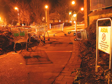Abandoned shopping trolleys on a pavement at night beside an Asda sign