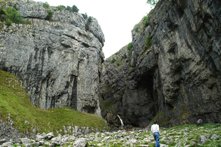 Person stands in a rocky valley beneath tall limestone cliffs