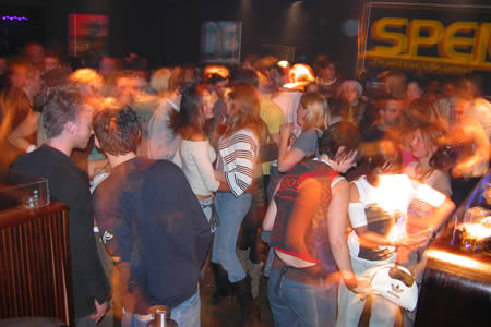 A crowd of people packed together in a dimly lit bar, with blurred movement