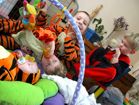 Children and babies in tiger-striped outfits play around a baby gym with colourful toys