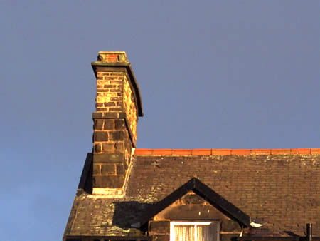 A chimney and slate roof with a dormer window against a blue sky