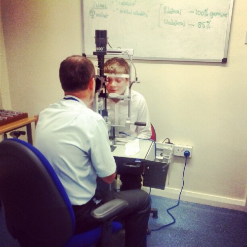 Person in a white shirt examines a child's eyes using a slit lamp at an eye clinic