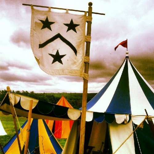 Medieval-style tents and a flag with two stars and a chevron against a cloudy sky