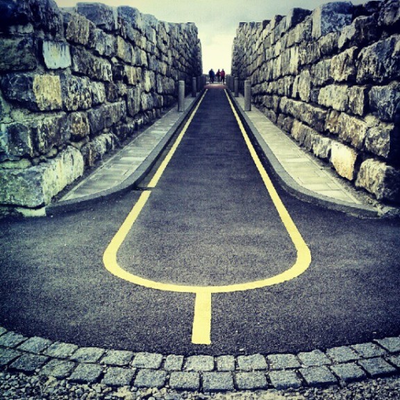 Narrow road with a yellow line curving in a loop between two stone walls