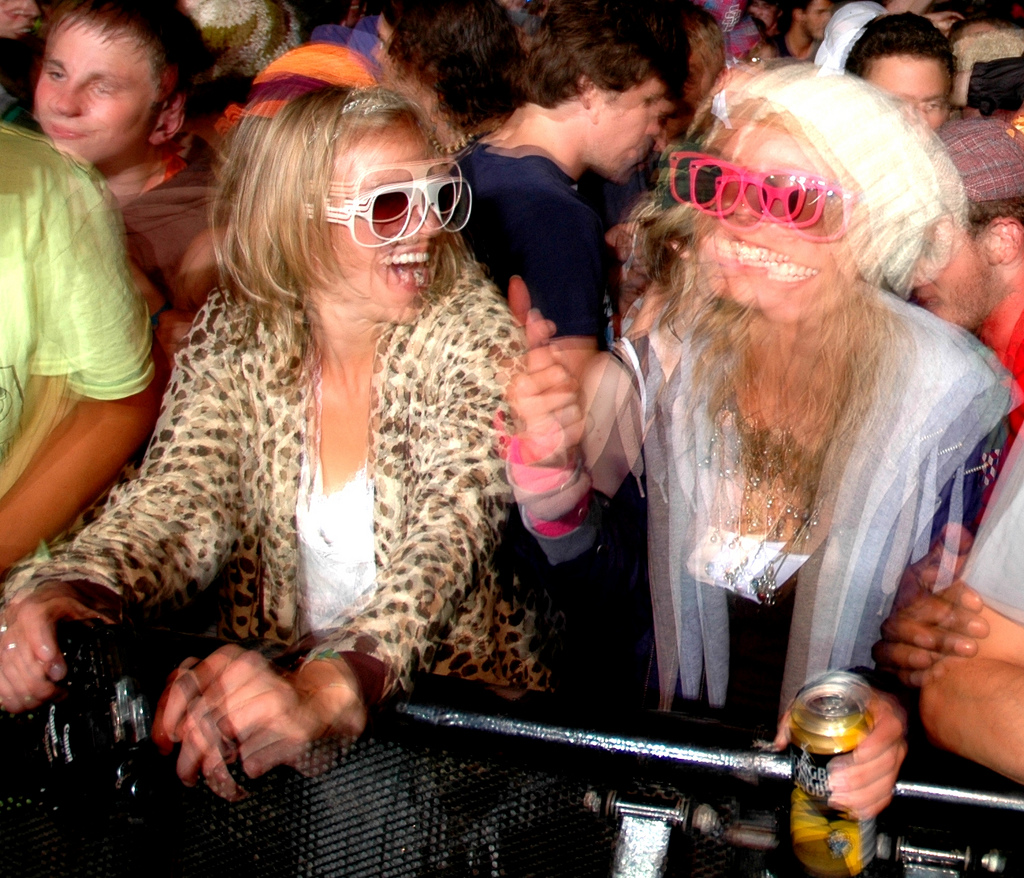 Crowd at a barrier, two people laughing in novelty glasses, one in a leopard print coat