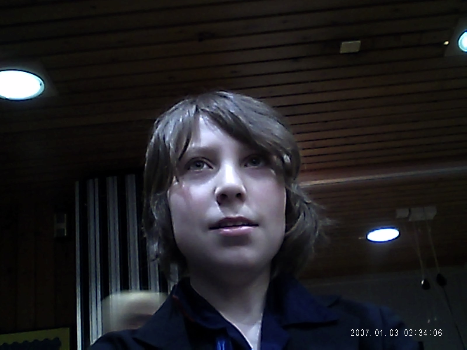 Child with dark brown hair looks up in a dim room, date stamp 2007 01 03
