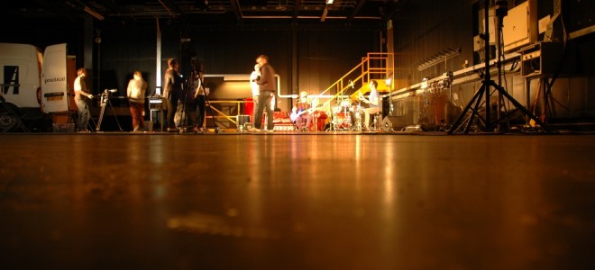 Low view of a polished warehouse floor with people and a drum kit at the far end