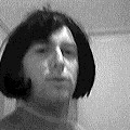 A man with a dark bob wig looks into the camera, black-and-white