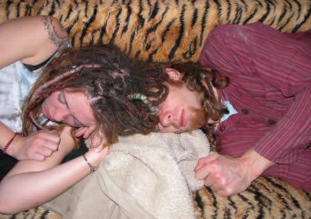 Person with dreadlocks asleep on a tiger-print sofa, with another person's arm beside
