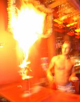A man behind a bar with a tall jet of flame rising from the counter